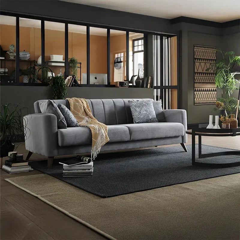 Gray sofa with a beige throw blanket and a patterned pillow, next to a wooden side table.